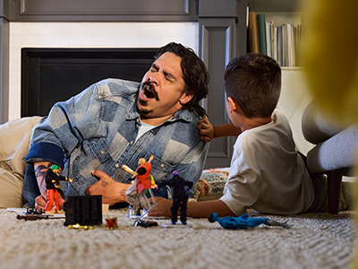 Man yawning while laying on the floor playing with his son