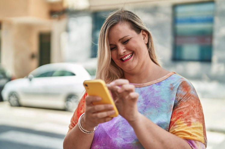 Una mujer mirando su teléfono y sonriendo.