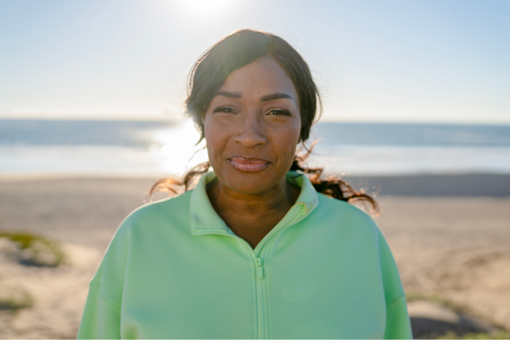 A woman smiling on the beach at sunset.