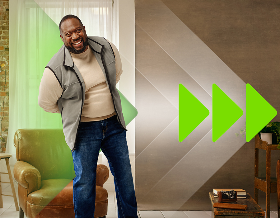 Image showing the side profile of a bearded man who is walking and wearing jeans and a tan sweatshirt. He is holding a tablet in his left hand and looking at the screen.